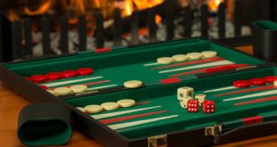 Ein aufgeklapptes Backgammon-Spiel mit mehreren Spielsteinen und Würfeln sowie einem Würfelbecher auf einem Tisch