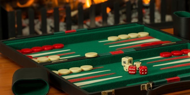 Ein aufgeklapptes Backgammon-Spiel mit mehreren Spielsteinen und Würfeln sowie einem Würfelbecher auf einem Tisch